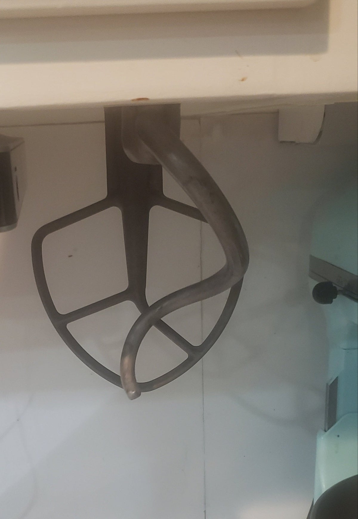 Metal stand mixer attachment hanging from a kitchen cabinet.