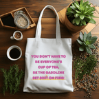 White tote bag with motivational quote on a wooden table with plants and coffee.
