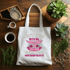 White tote bag with humorous design on a wooden table with plants and coffee.