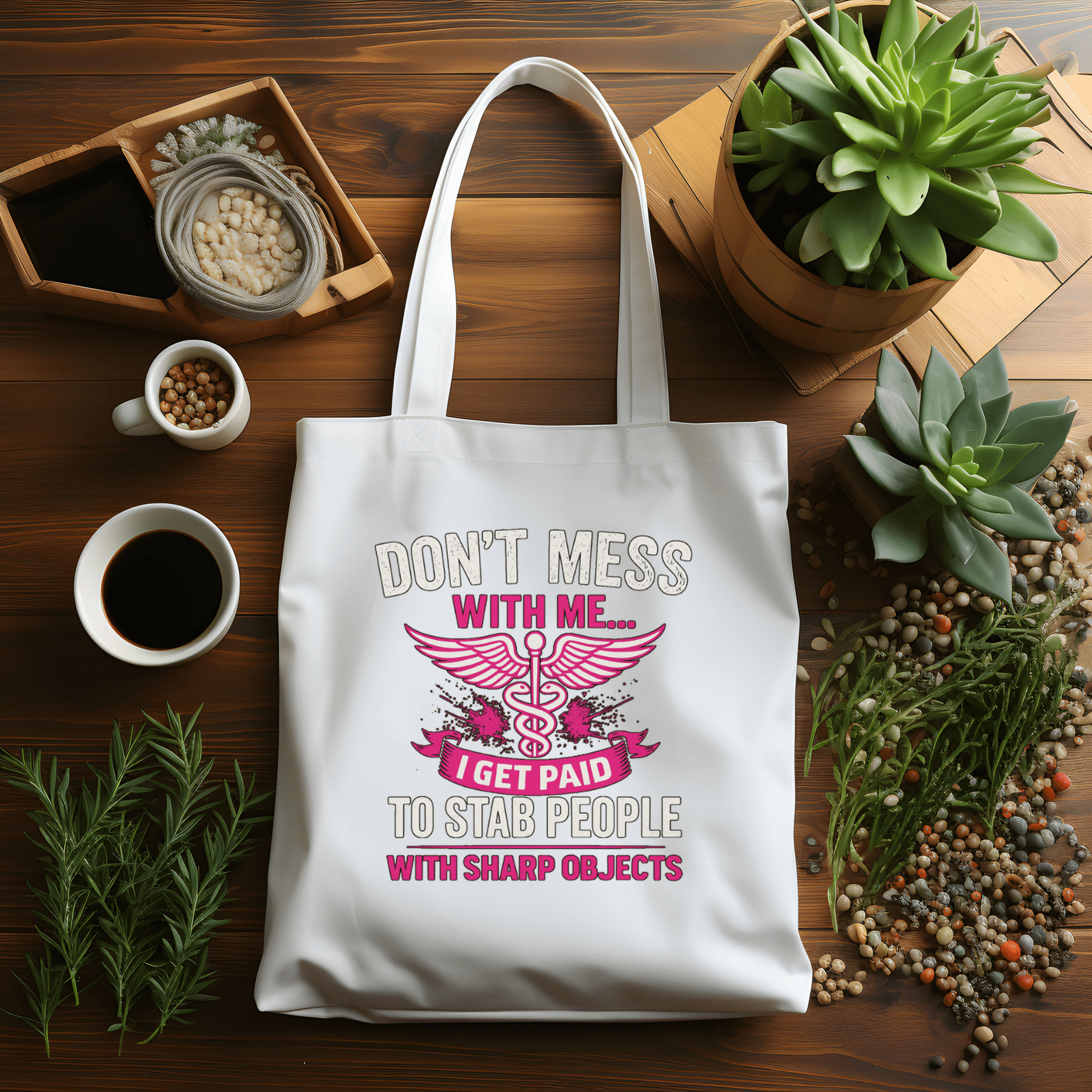 White tote bag with humorous design on a wooden table with plants and coffee.