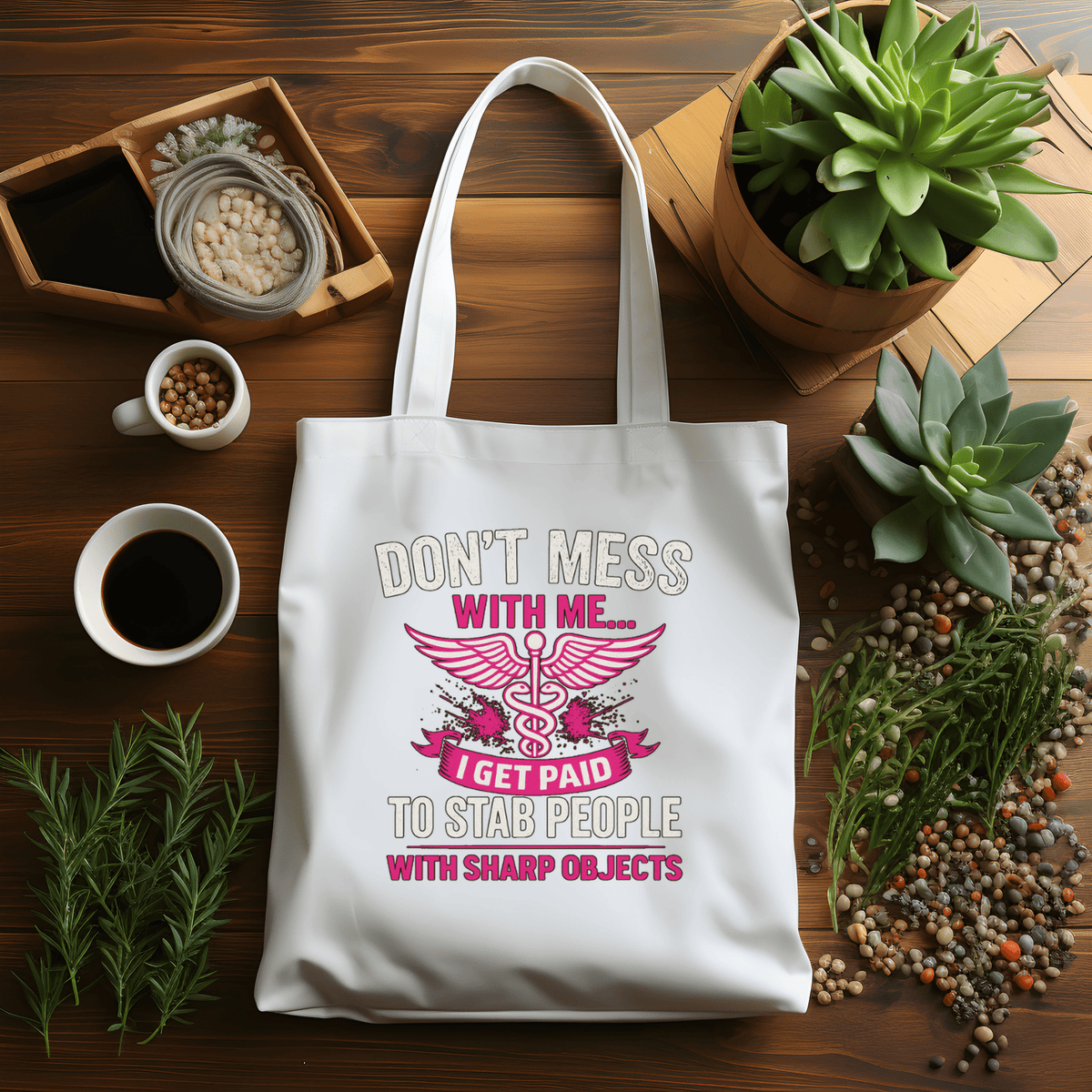 White tote bag with humorous design on a wooden table with plants and coffee.