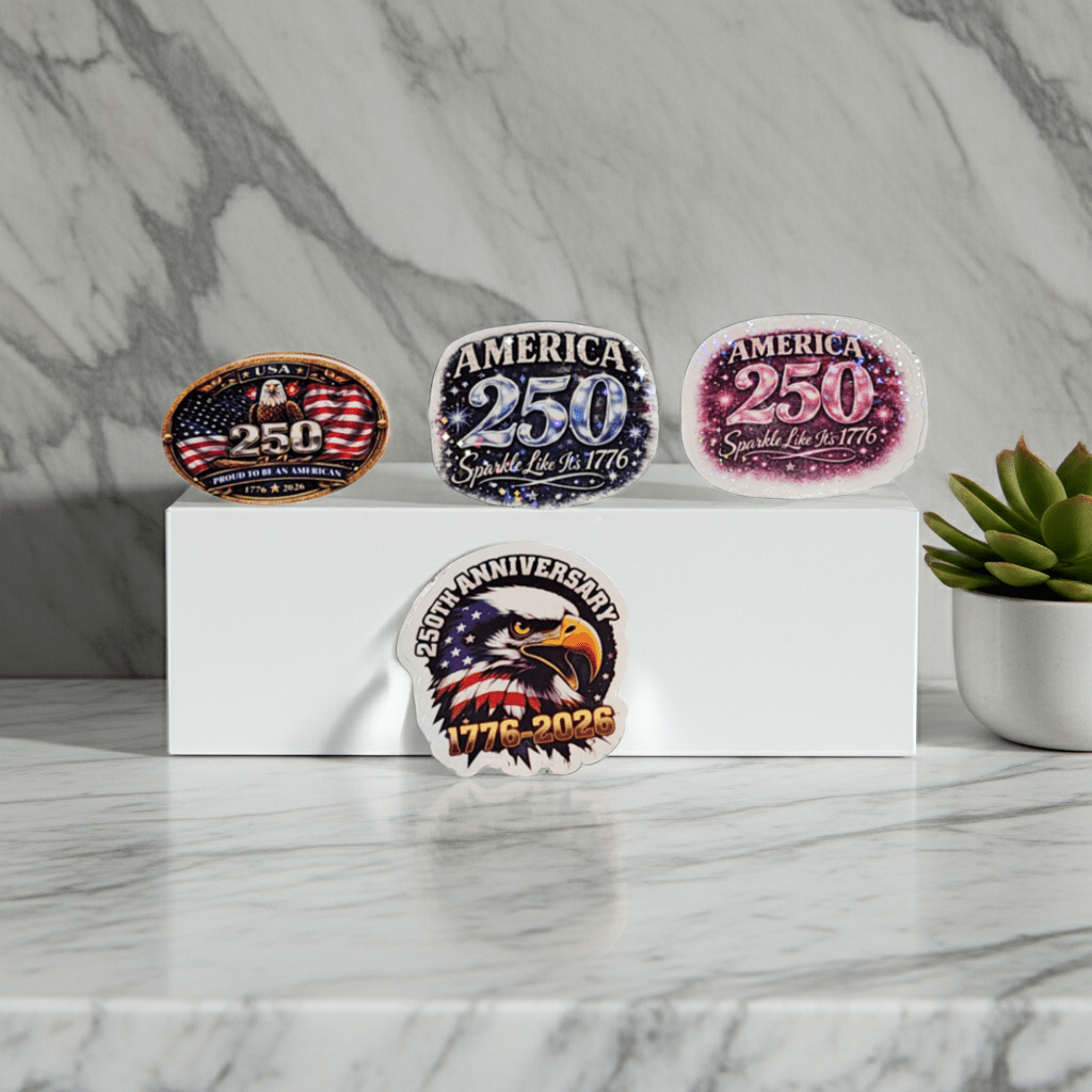 Four commemorative pins with 'America 250' and '1776-2028' text on a marble surface.
