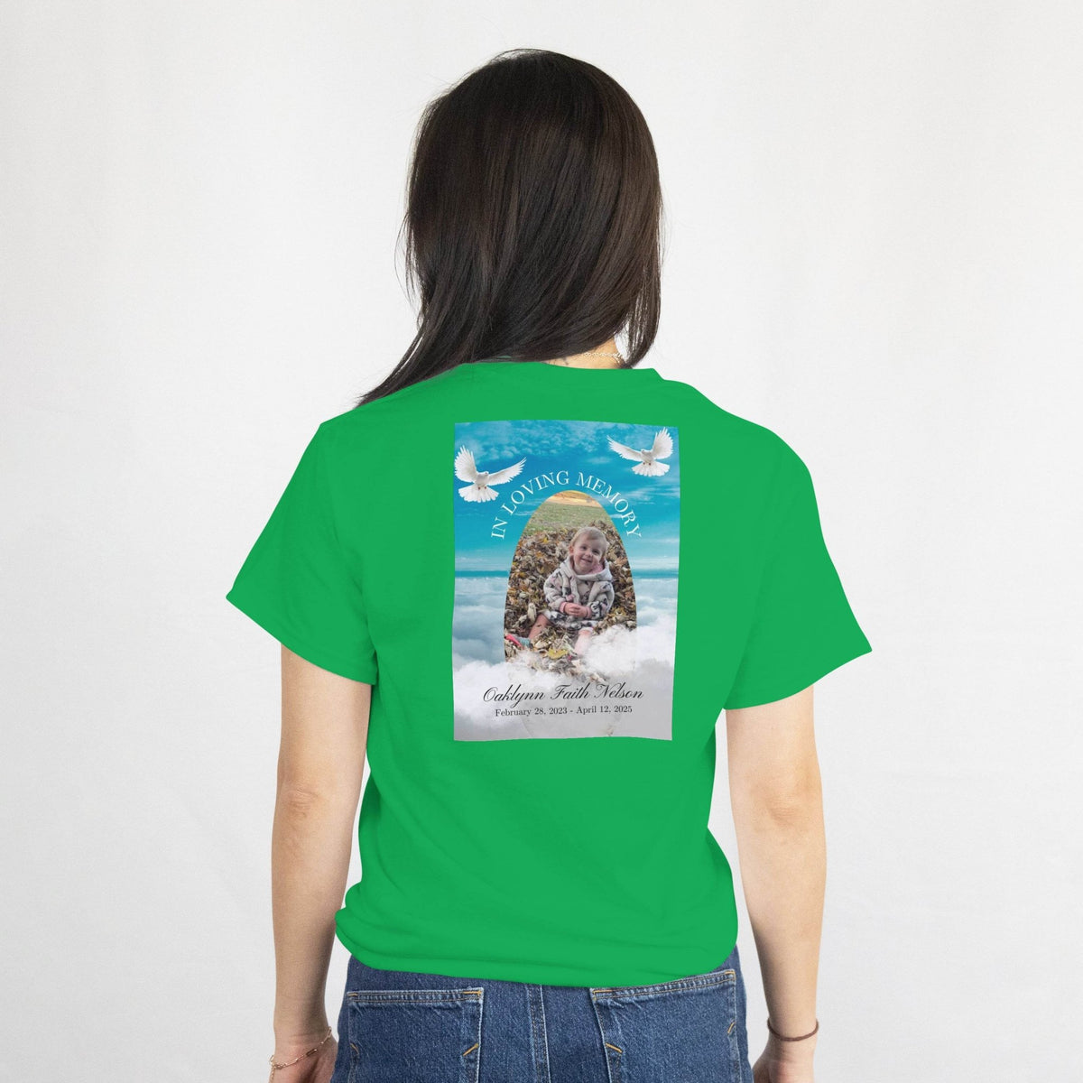 Back view of a green memorial T-shirt with a photo, arch, doves, and In Loving Memory, featuring name and dates.