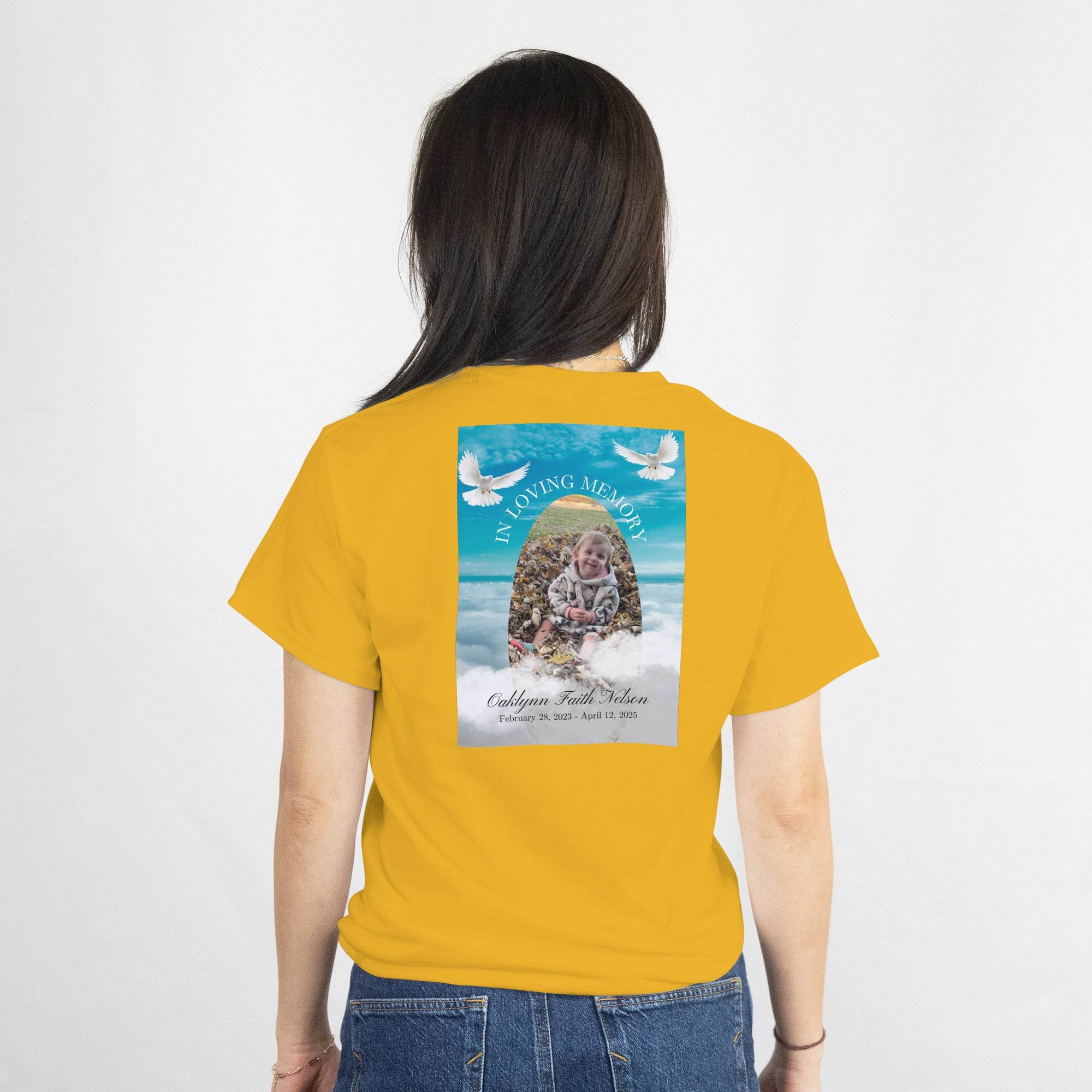 Mustard memorial T-shirt back print featuring a photo, name, dates, an arch, and gentle doves against a blue sky.