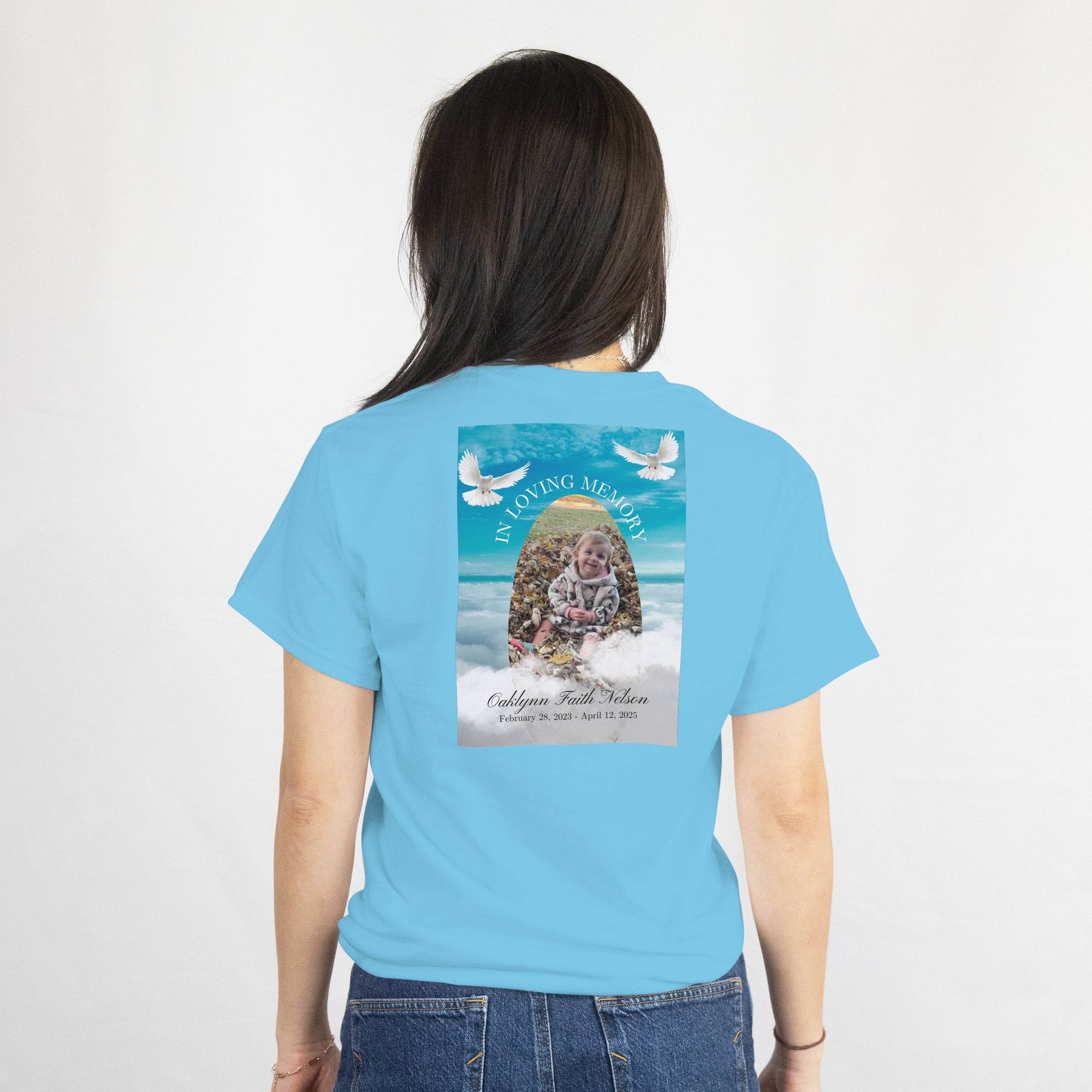Back of blue T-shirt memorial design with a baby photo, two doves, and 'In Loving Memory' arch, name and dates.