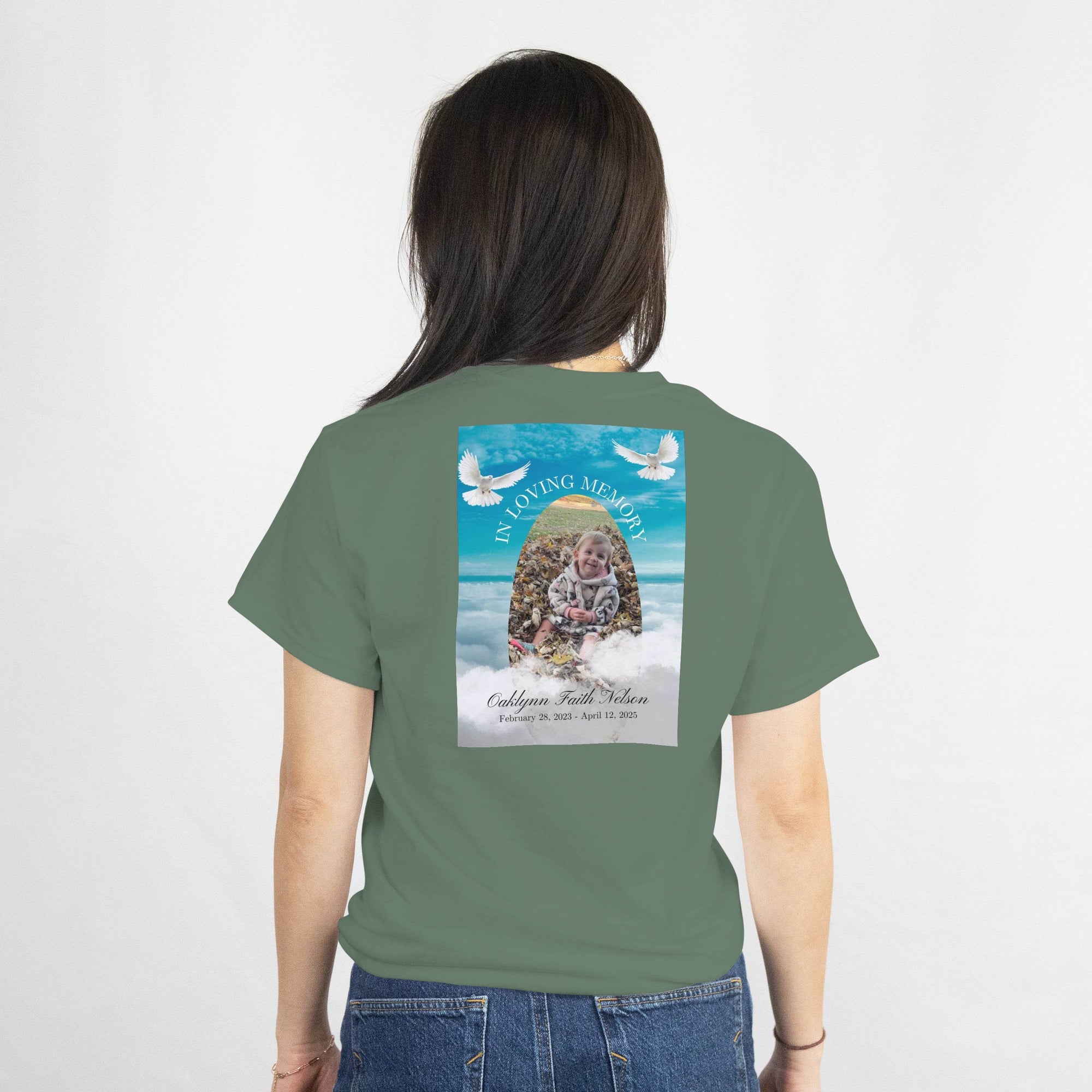 Back of olive-green tee with In Loving Memory memorial design: photo, name, dates, and white doves in the sky.