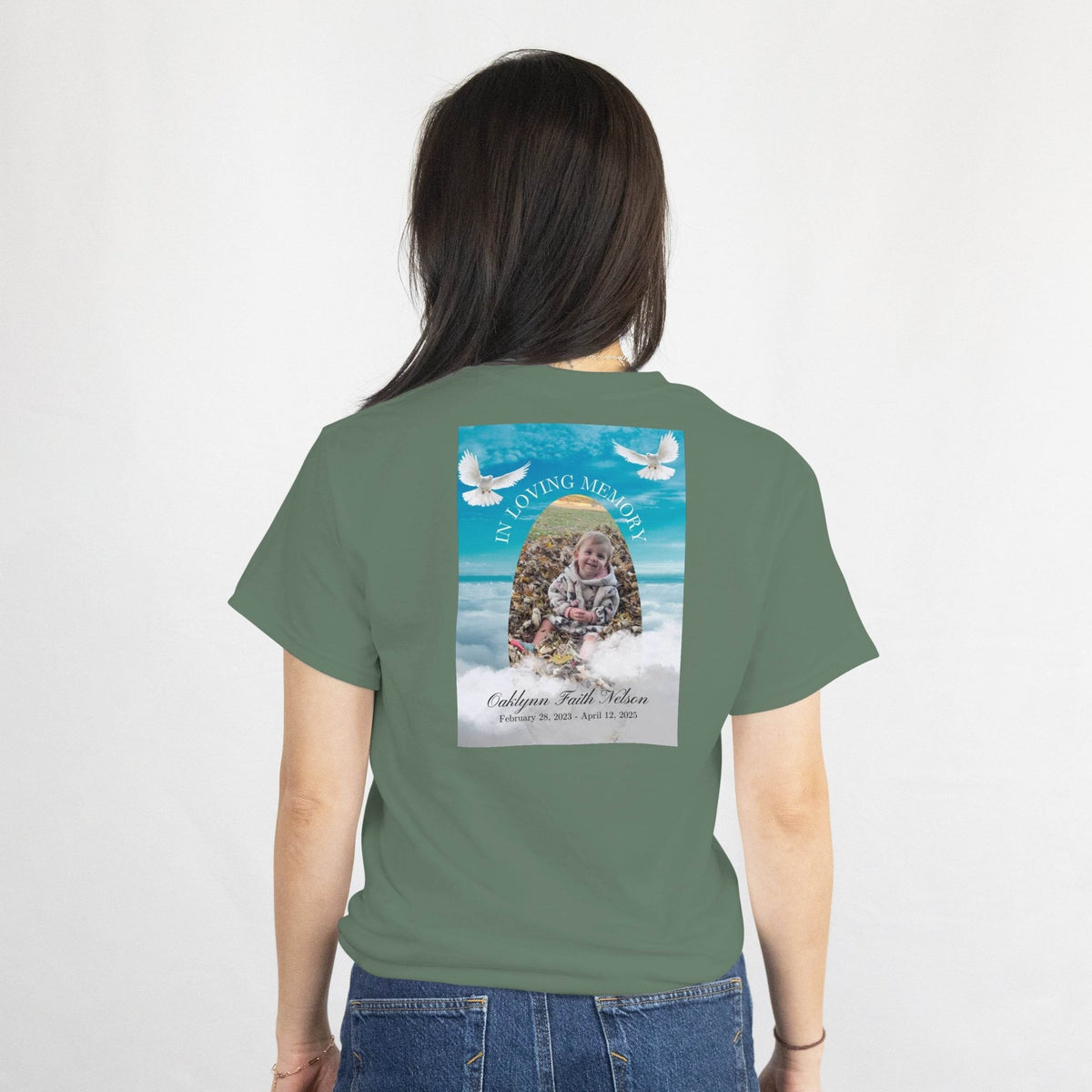 Back of olive-green tee with In Loving Memory memorial design: photo, name, dates, and white doves in the sky.