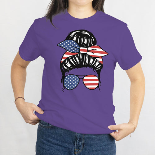 Gildan Patriotic Messy Bun T-Shirt with a messy bun, USA flag bandana, and star-spangled sunglasses on a purple tee.