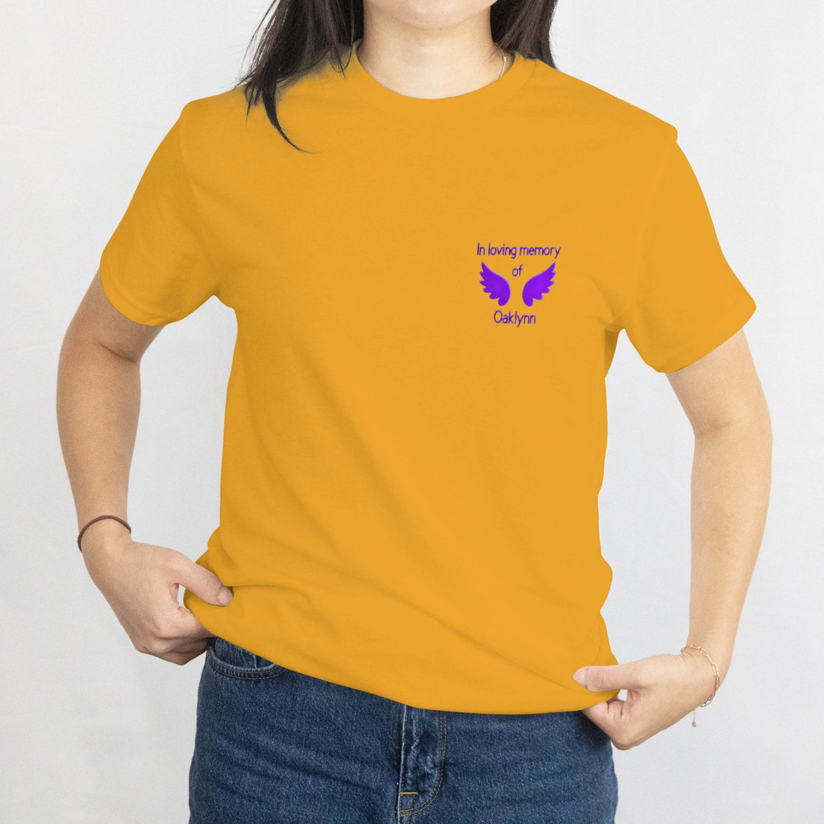 Mustard T-shirt with a small purple memorial design on the front reading In loving memory of Oaklynn with dove wings.