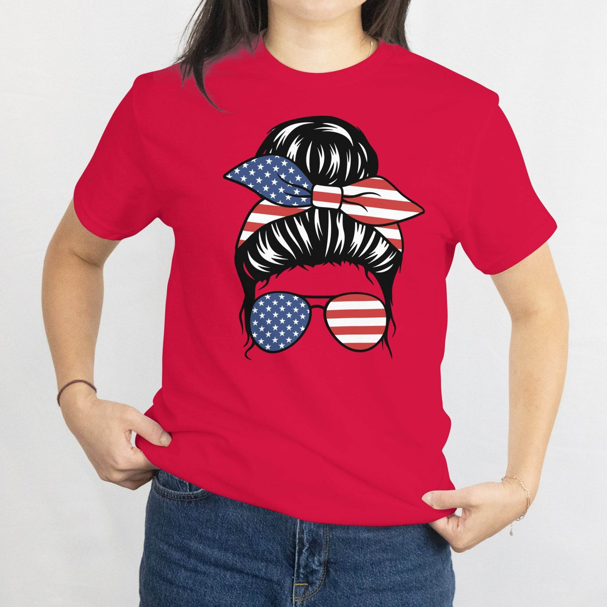 Red Gildan Patriotic Messy Bun T-Shirt with a bun, star-spangled bandana, and American flag sunglasses graphic.