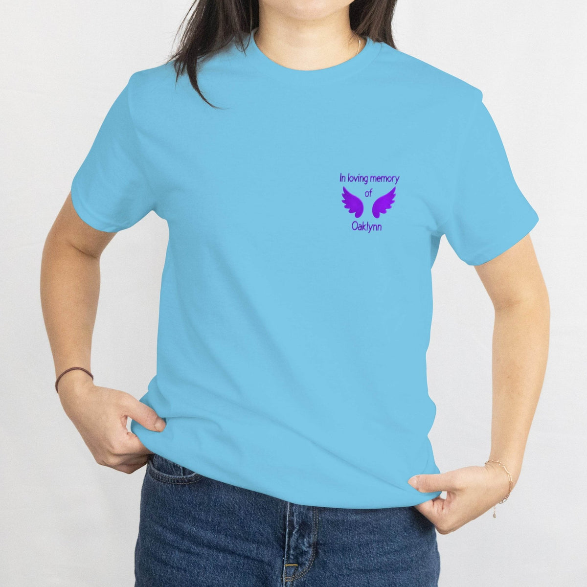 Light blue T-shirt with a purple memorial design on the left chest, 'In loving memory of Oaklynn' with wings.