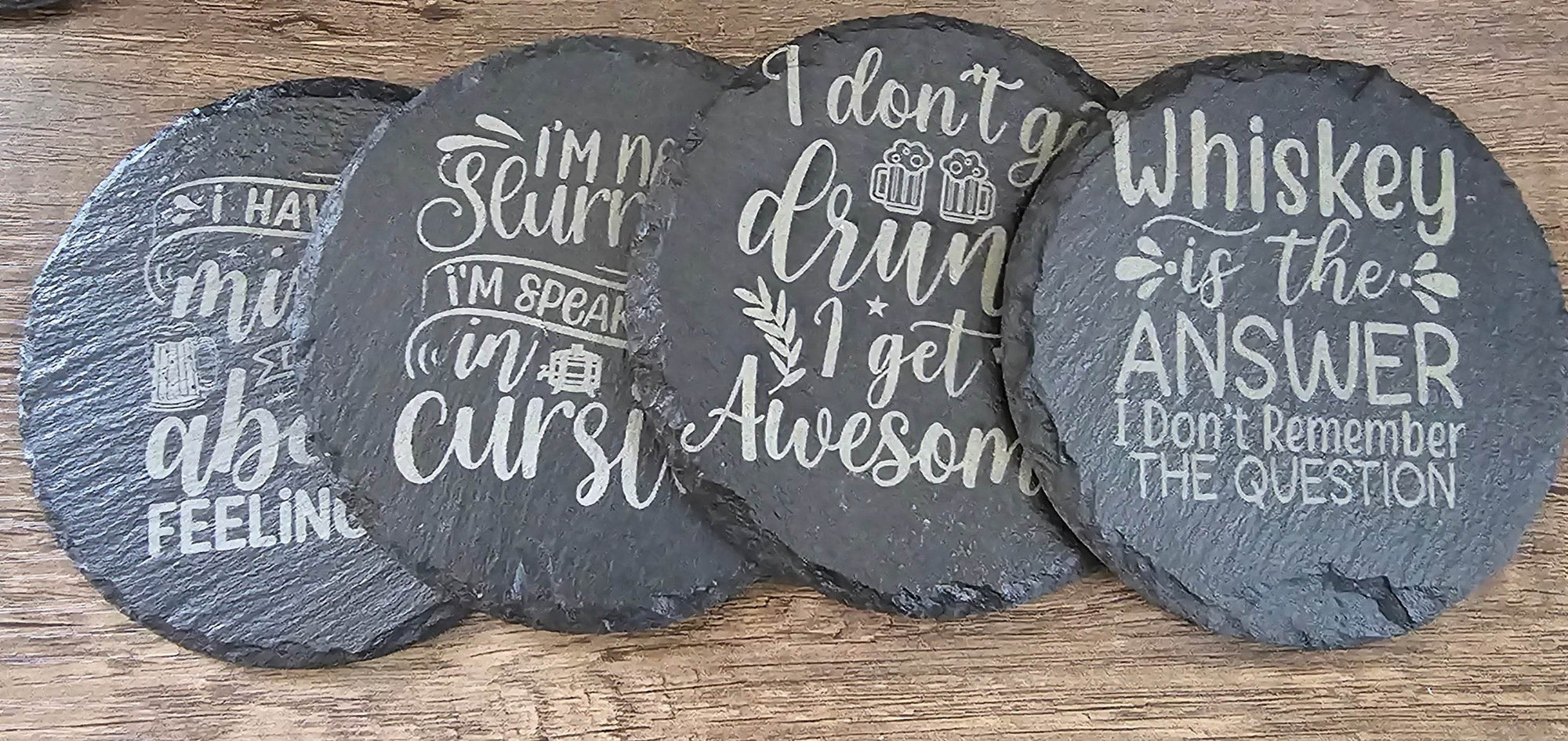Set of four round black slate coasters with white engraved quotes for a stylish home bar.