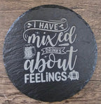 Round black slate coaster with white chalk-style typography reading I have mixed drinks about feelings.