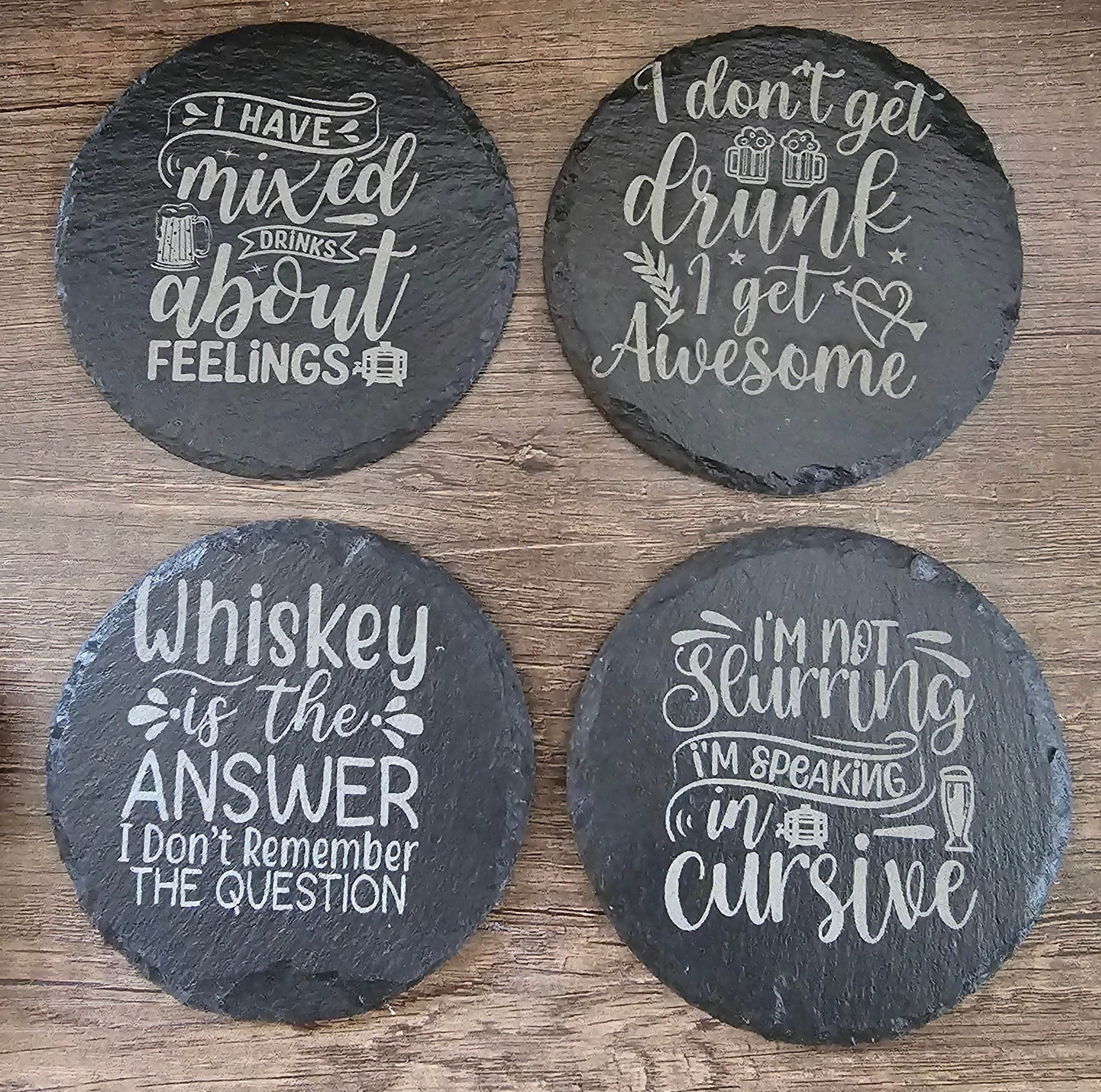 Four round black slate coasters with white chalk-style drink quotes.