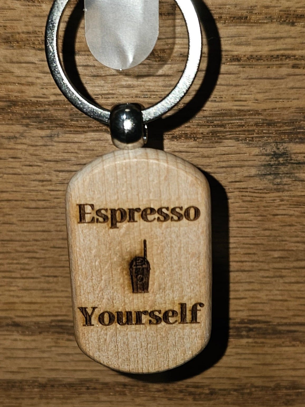 A wooden espresso-themed keychain tag engraved with 'Espresso Yourself' and a small espresso cup icon, hanging from a metal ring on a wooden surface.