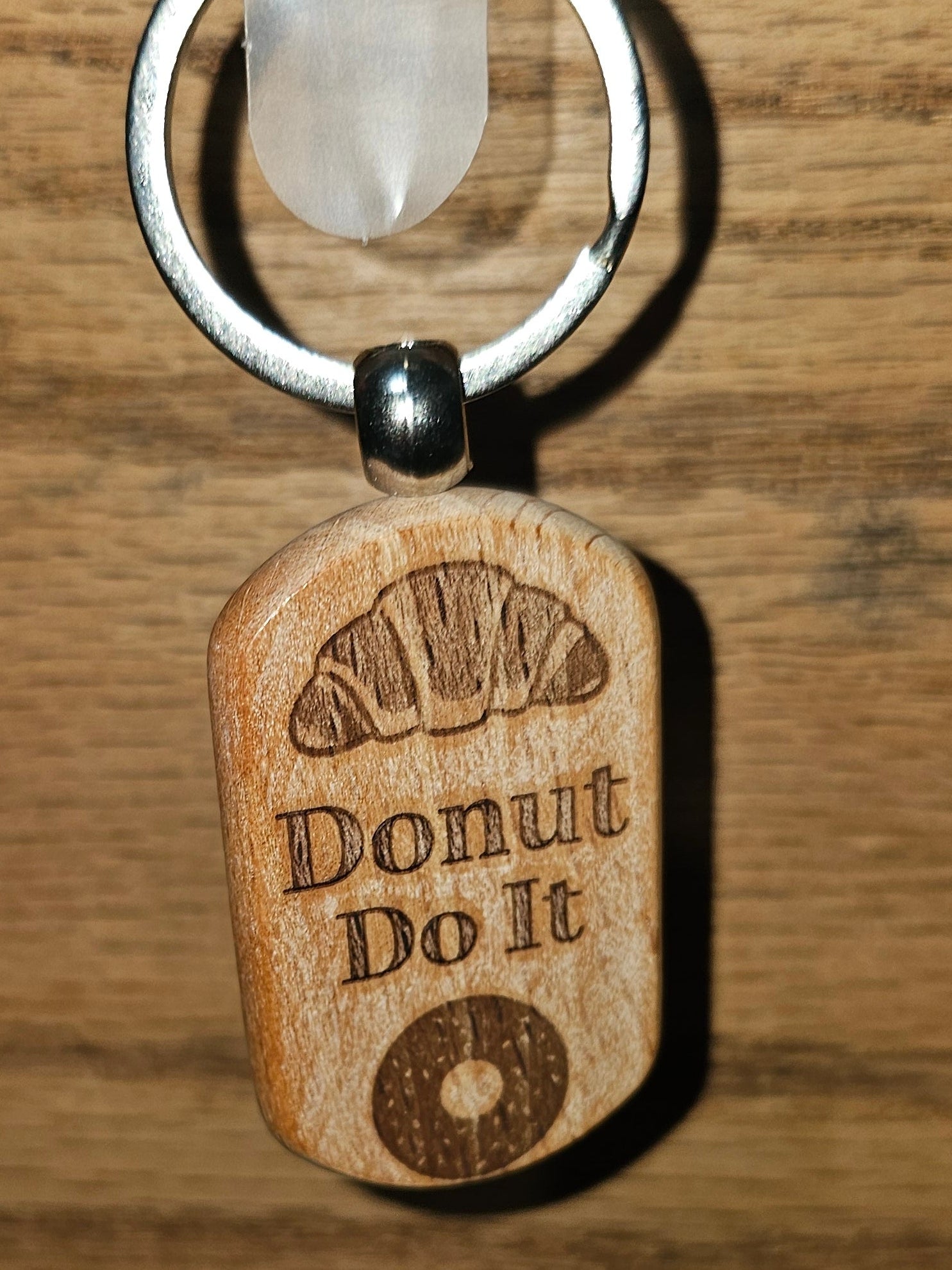 A wooden engraved keychain tag with the words 'Donut Do It' and a donut graphic, attached to a silver metal ring and hanging against a wood-grain background.