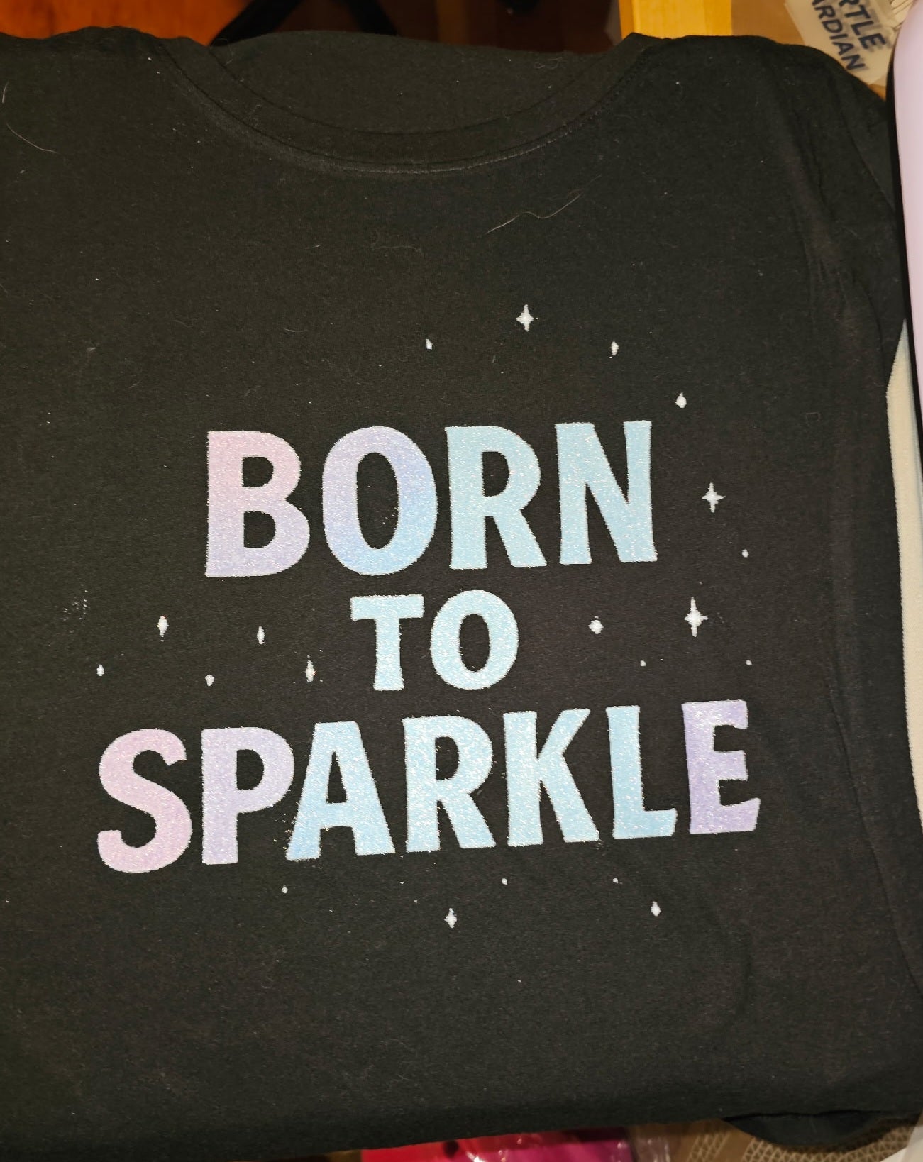 Black shirt with 'Born to Sparkle' text in pastel colors on a dark background