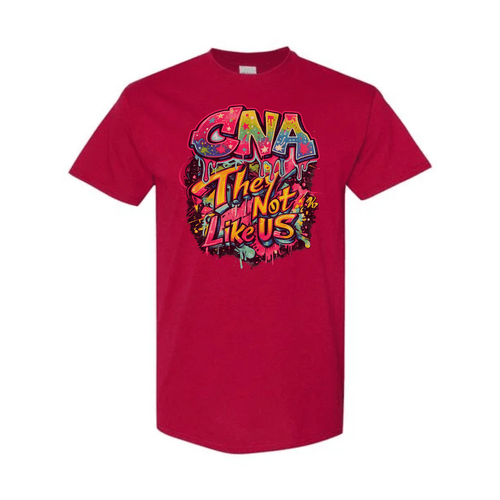 A red short-sleeve crewneck t-shirt featuring a colorful graphic on the chest that reads 'CNA They Are Not Like Us' in a graffiti-style font with pink, yellow, and blue tones.
