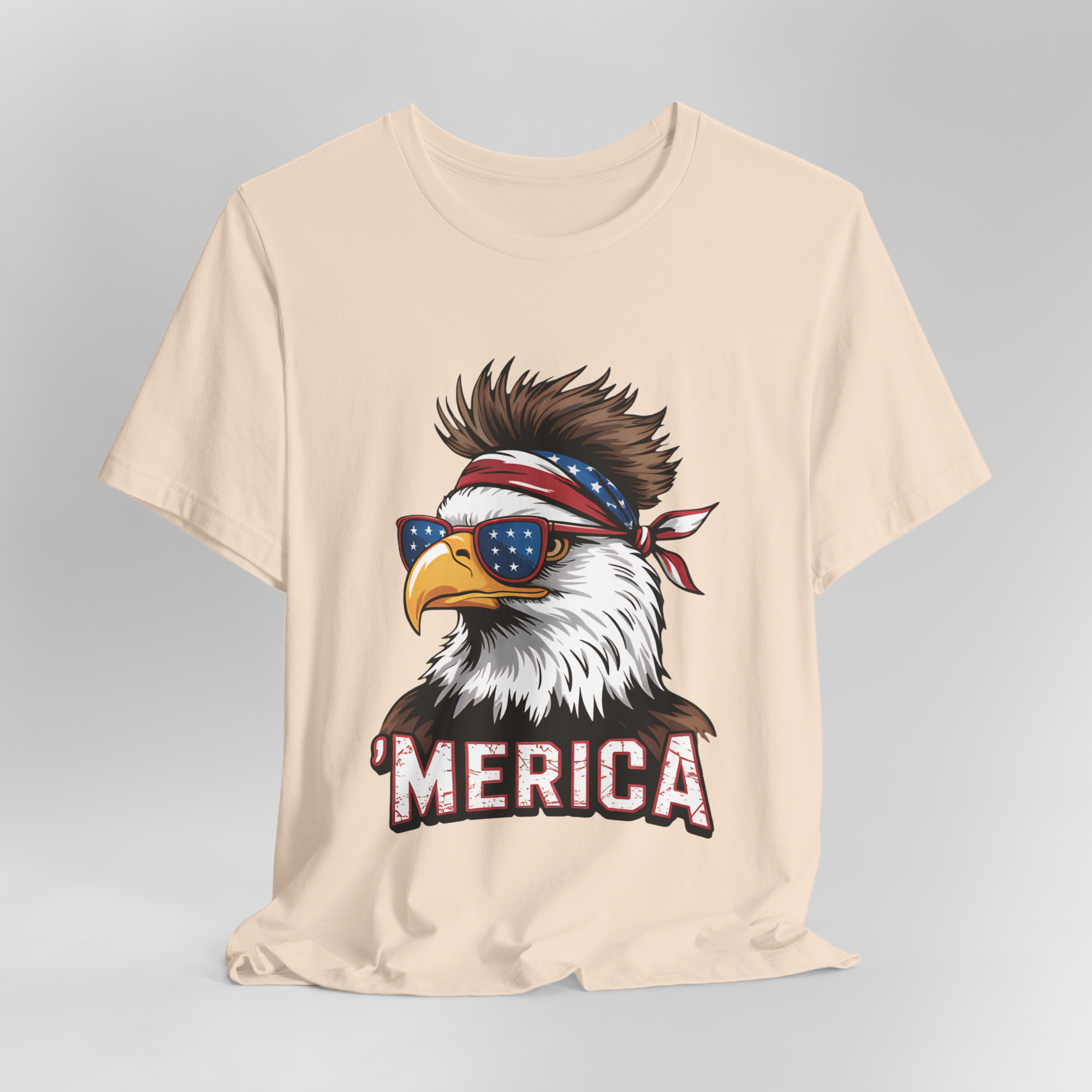 Beige T-shirt featuring a bold eagle graphic wearing star-spangled sunglasses and a bandana with MERICA text