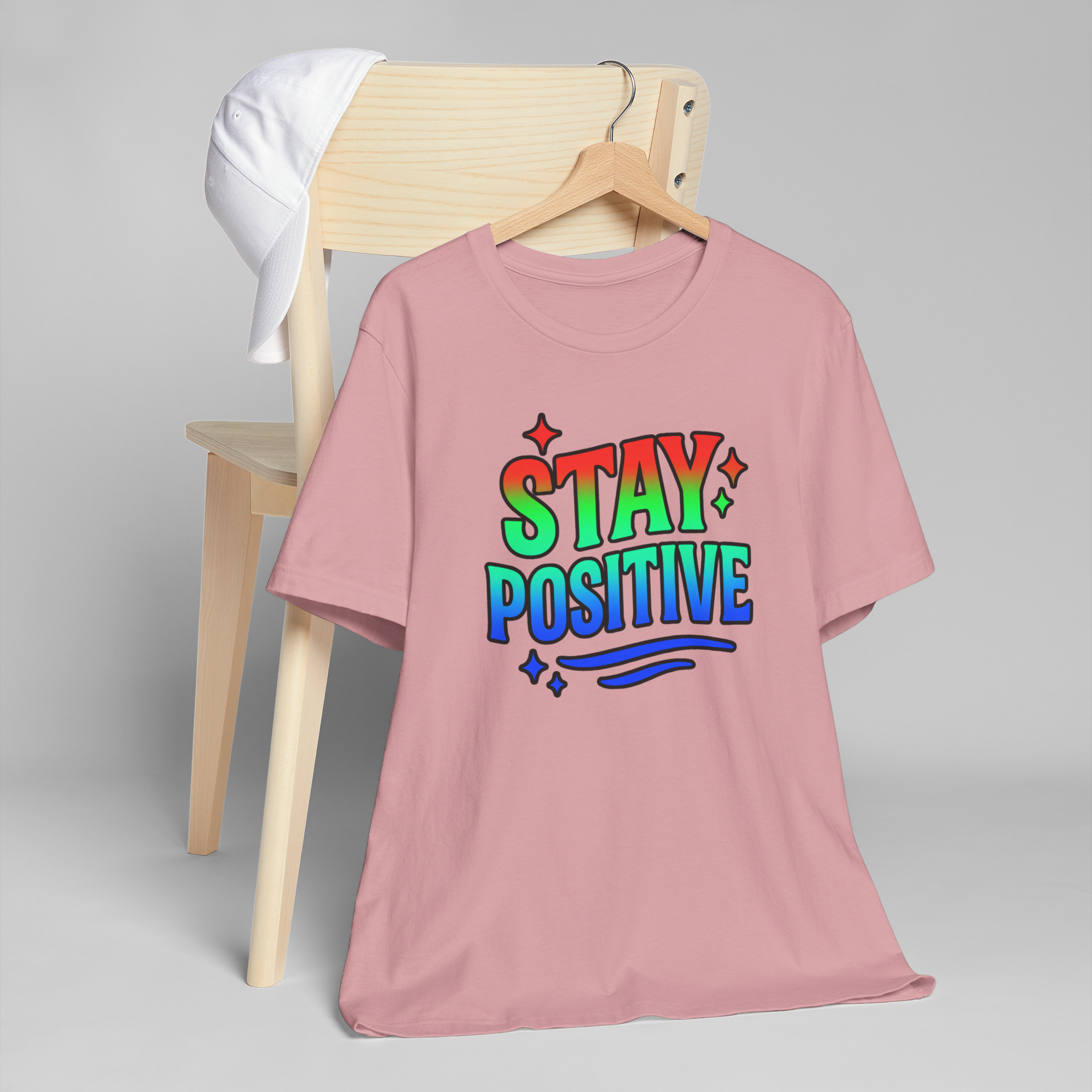 Stay Positive pink T-shirt with rainbow gradient lettering and star accents.