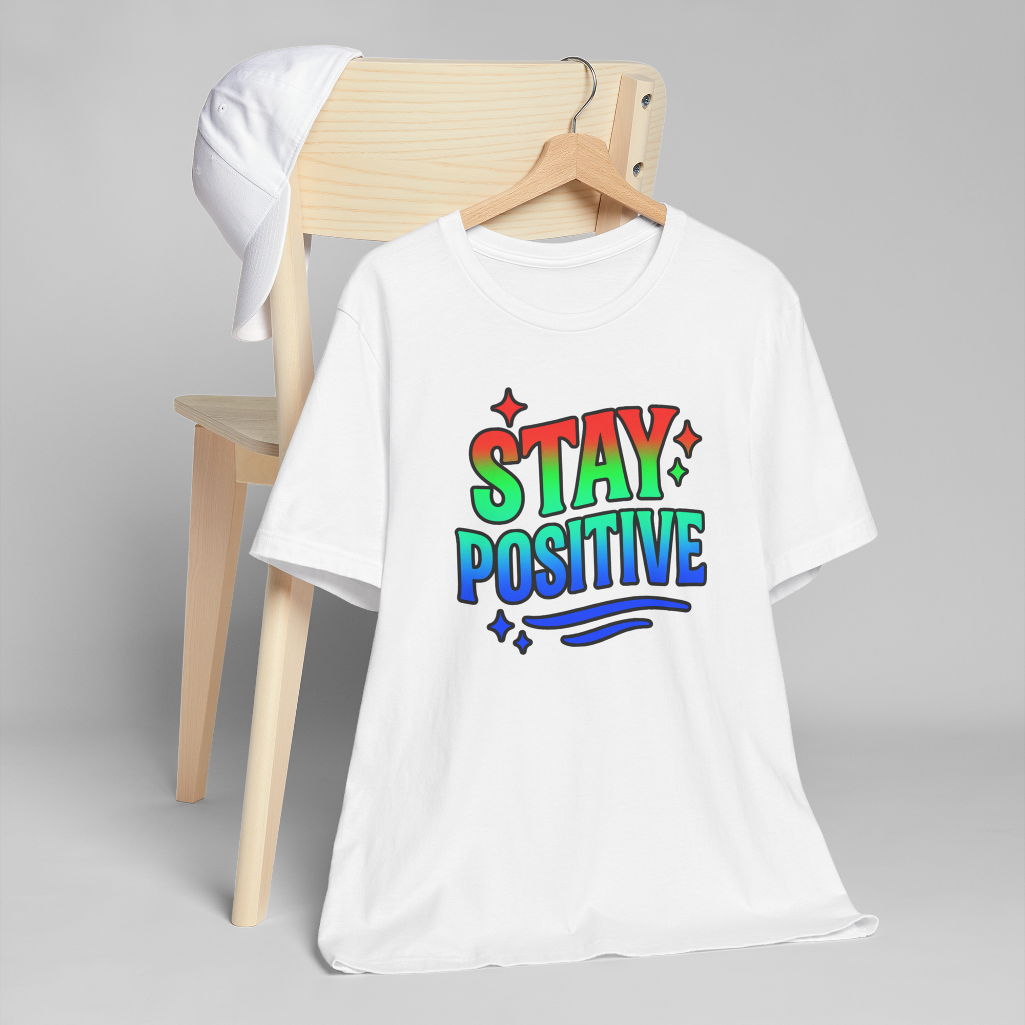 Stay Positive rainbow-gradient text on a white T-shirt with stars and decorative swirls.