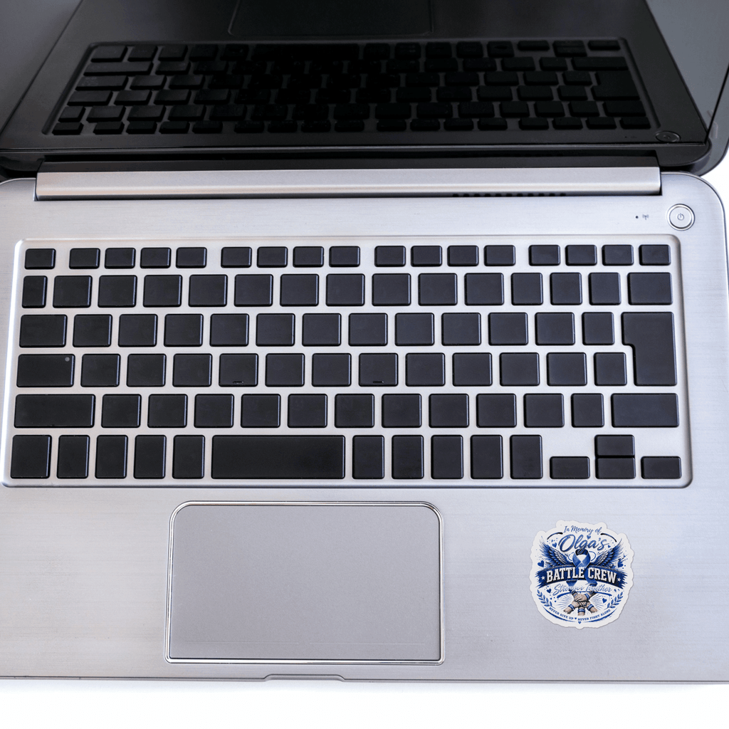 Sticker In Memory Of Olga on a silver laptop, blue memorial badge reading In Memory Of Olga's Battle Crew.