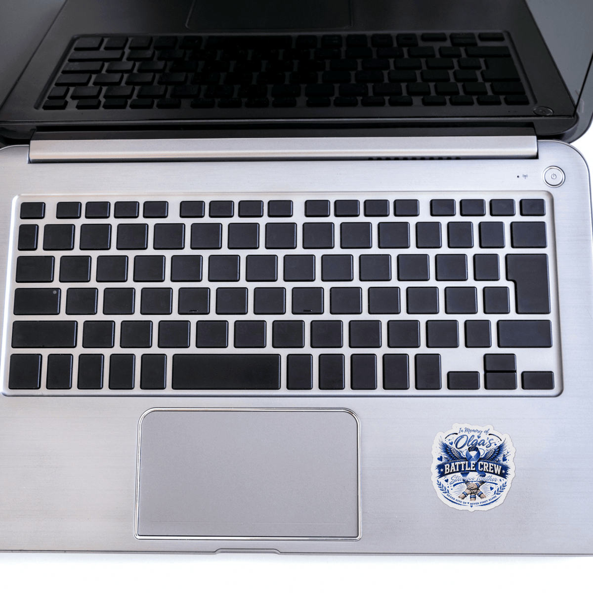 Sticker In Memory Of Olga on a silver laptop, blue memorial badge reading In Memory Of Olga's Battle Crew.