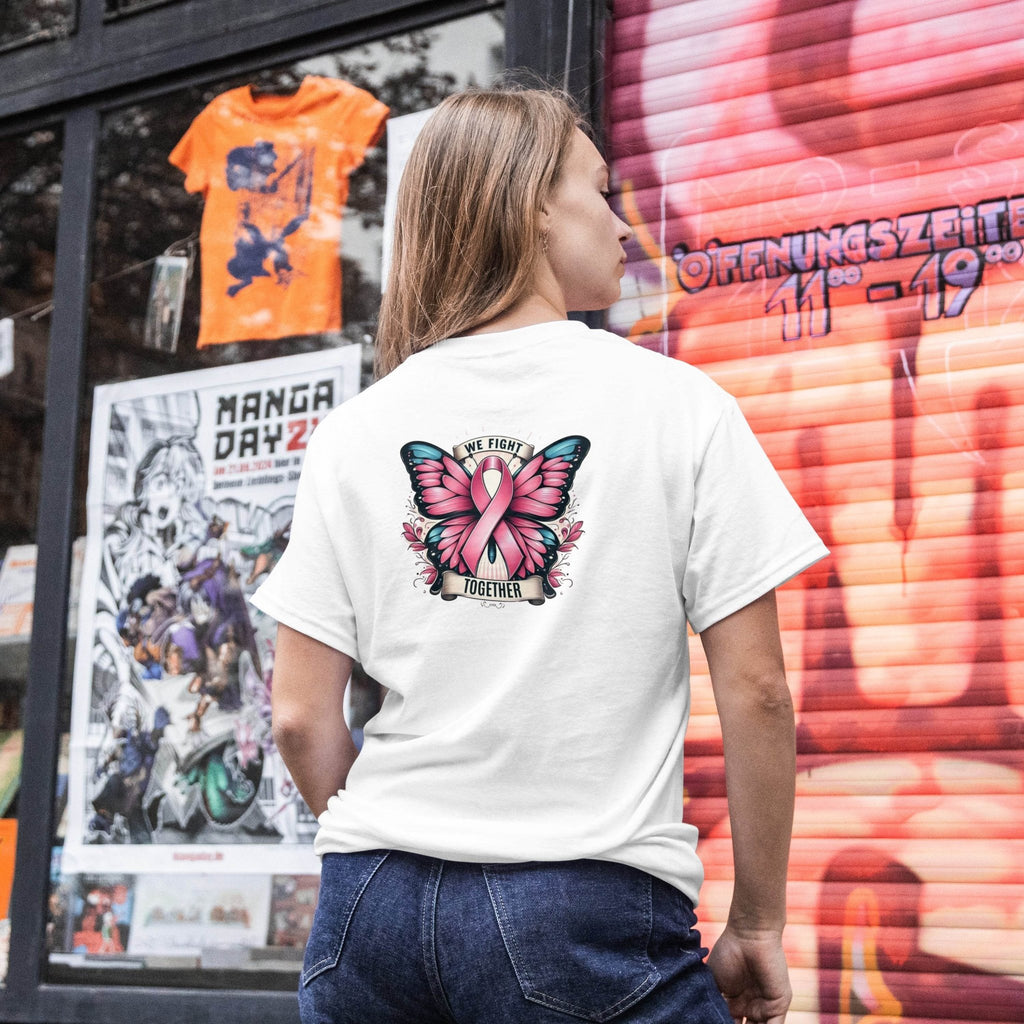 Person wearing a white t-shirt with a butterfly design and pink ribbon, standing in front of a colorful store window.
