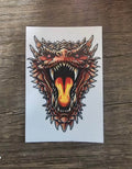 Colorful dragon tattoo design on a white card with a wooden surface background