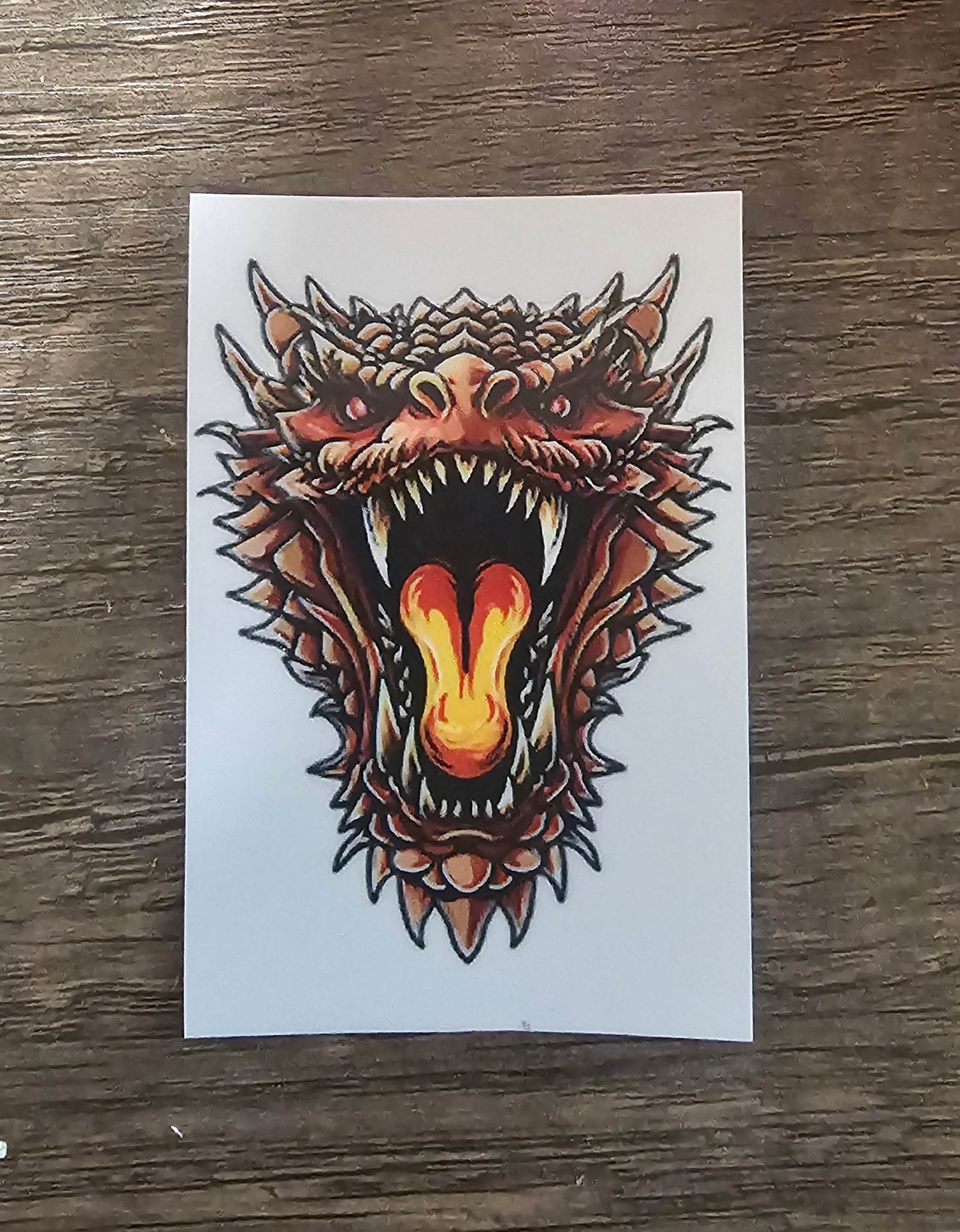 Colorful dragon tattoo design on a white card with a wooden surface background