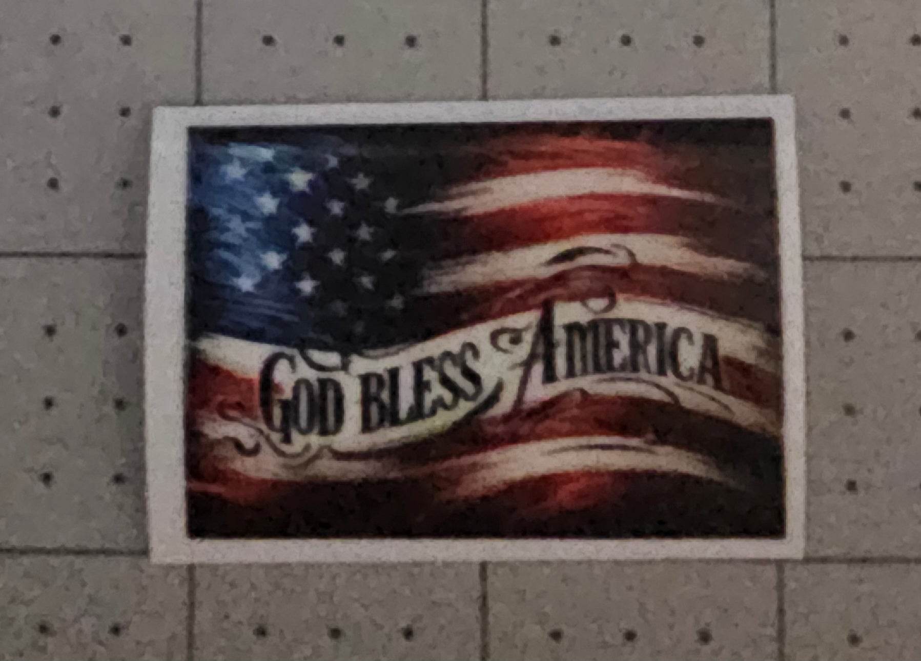 American flag with 'God Bless America' text on a gray pegboard background
